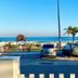 Hostel Dos Gringos in Maricá with parked cars, palm trees, and ocean view toward a lifeguard tower