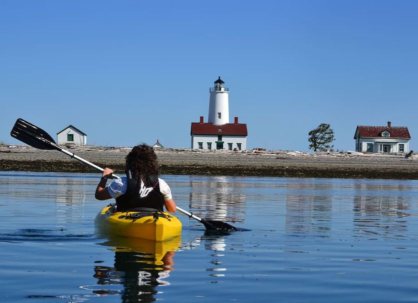 Juan de Fuca Waterfront Hotel & Cottages in Sequim: kayaker on calm water with lighthouse and cottages
