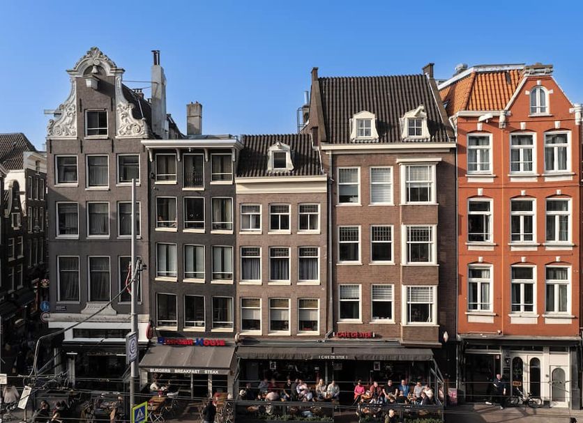 Cs Hotel Amsterdam canal-side row buildings with outdoor cafe seating and clear blue sky