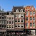 Cs Hotel Amsterdam canal-side row buildings with outdoor cafe seating and clear blue sky