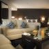 Asdal Boutique Hotel Seef Manama suite with beige sofa, coffee table, minibar setup, and modern lighting