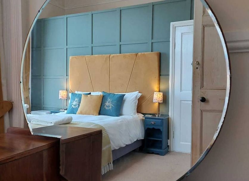 Laston House Ilfracombe bedroom with round mirror reflecting a bed, blue paneled wall and bedside lamps