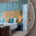 Laston House Ilfracombe bedroom with round mirror reflecting a bed, blue paneled wall and bedside lamps