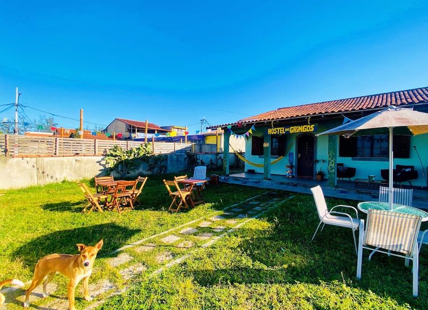Hostel Dos Gringos in Maricá with a sunny garden patio, outdoor tables, and a dog in the yard