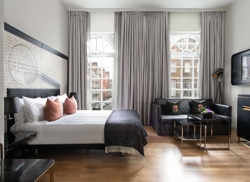 Holmes Hotel London guest room with king bed, lounge chairs and large street-facing windows in London