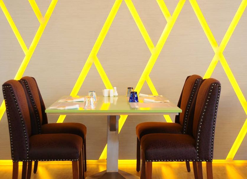 One One Bangkok Hotel dining table with two brown chairs and geometric yellow-lit wall