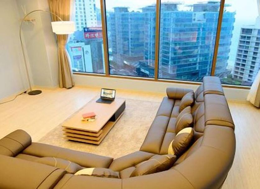 Marianne Hotel Busan lounge with curved sofa, floor lamp and city view through large windows