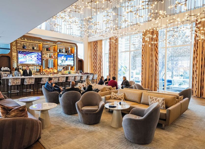 HALL Arts Hotel, Dallas lobby lounge with bar seating, plush chairs, and tall windows