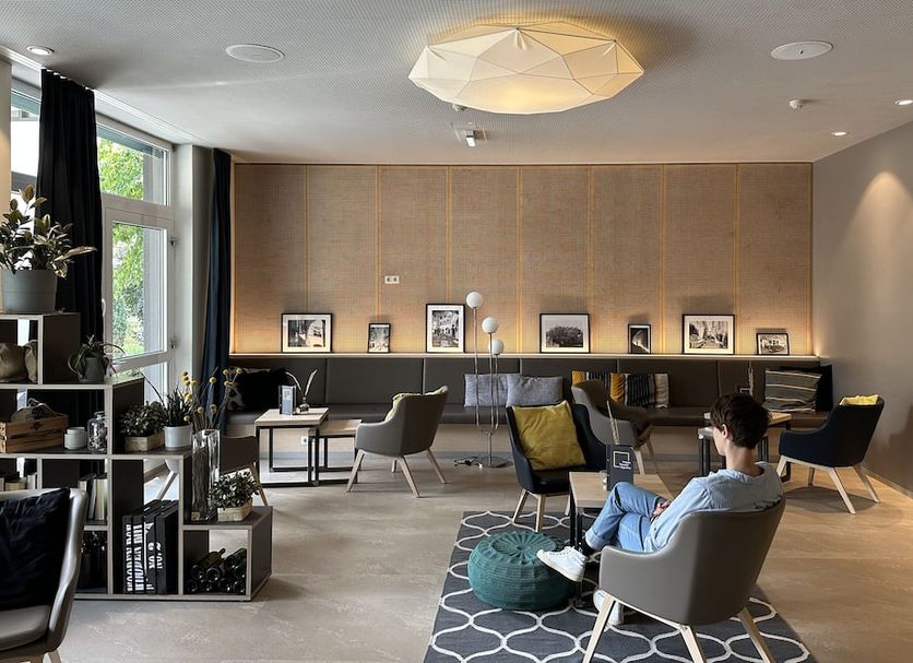 JUFA Hotel Graz lounge with chairs, low table, shelves, and large windows in Graz
