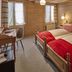 Baeren Wilderswil guest room with twin wooden beds, red throws, desk, and window with sheer curtains