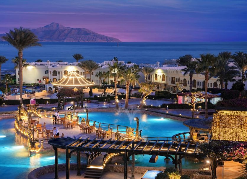Charmillion Club Resort in Sharm el-Sheikh with a lit pool, palm trees, and sea view at dusk