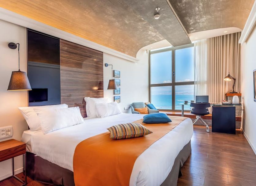 Nof Hotel in Haifa guest room with large ocean-view window, bed, desk, and blue seating