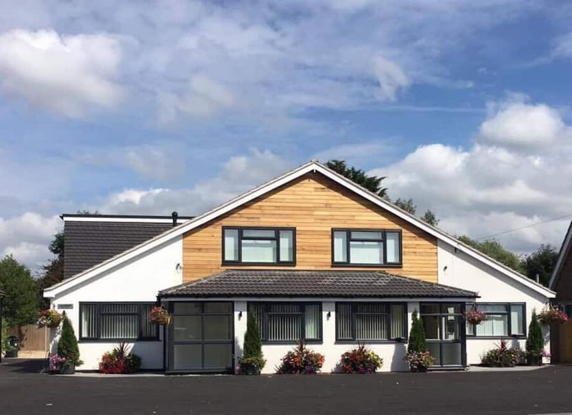 The Dakota Guesthouse Baginton in Coventry, a white and wood guesthouse exterior under a blue sky.