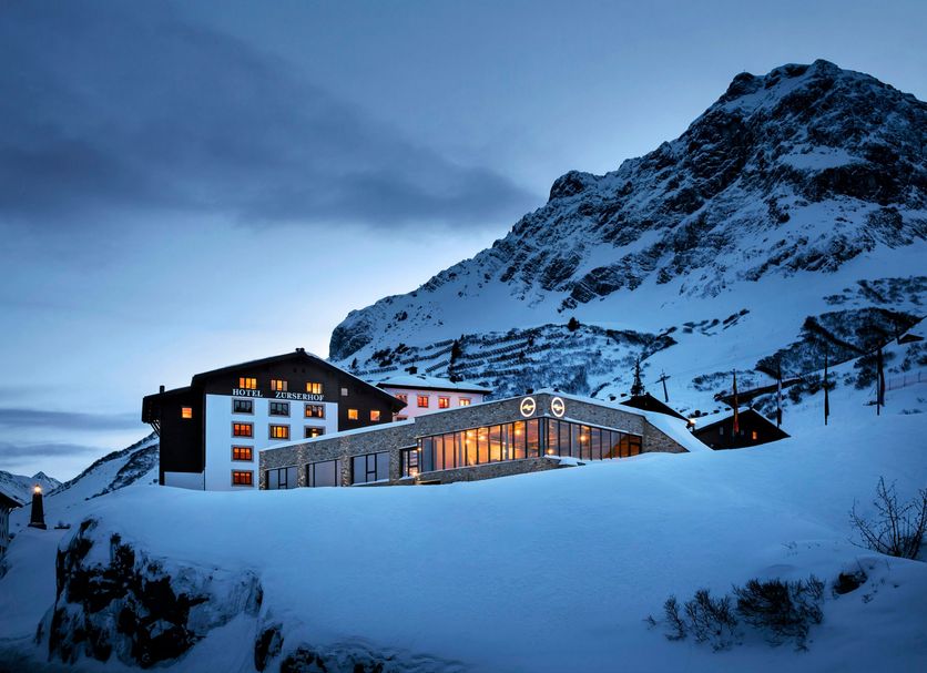 Hotel Zurserhof in Zürs at dusk, with a snow-covered mountain backdrop and illuminated windows