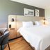 Campanile Nature - Mont De Marsan guest room with king bed, open closet and chair in Mont-de-Marsan