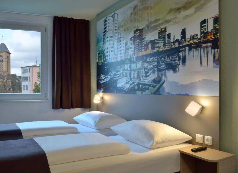 B&B Hotel Düsseldorf City-Süd guest room with twin beds, city mural, and window view in Düsseldorf