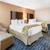Baymont by Wyndham Port Arthur/Groves Area guest room with two beds, armchair, ottoman and desk