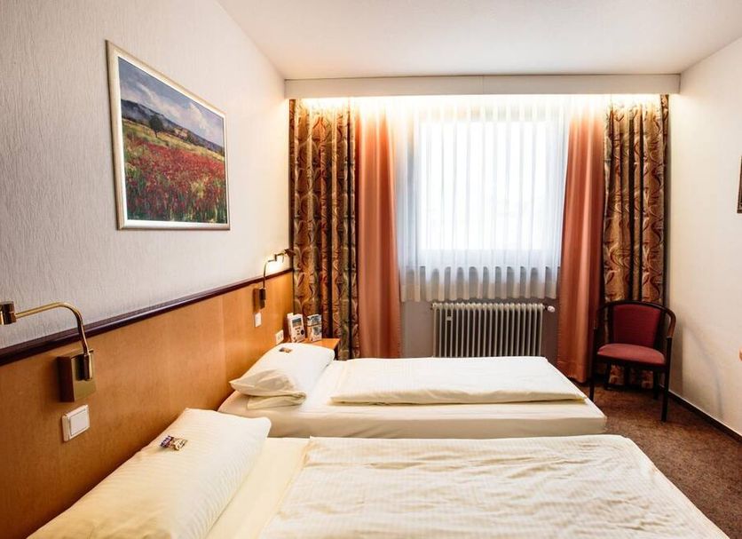 Hotel St. Pierre in Bad Hönningen guest room with two single beds, window, curtains, and chair