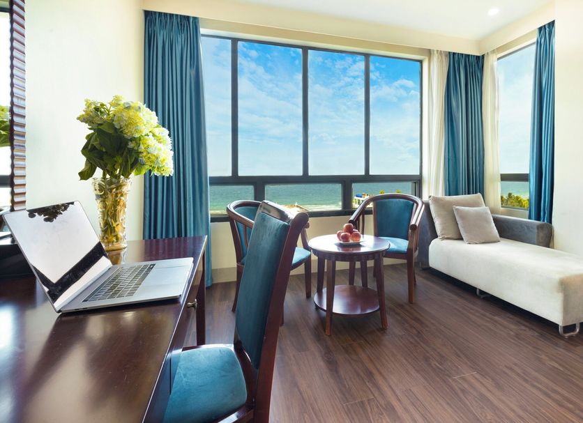 Seafront Hotel Danang in Da Nang room with ocean view, desk, chairs, and sofa by large windows