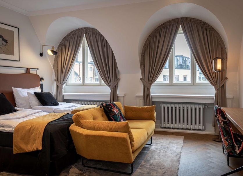 Scandic Grand Central Helsinki room with mustard sofa, bed, arched windows and city view in Helsinki