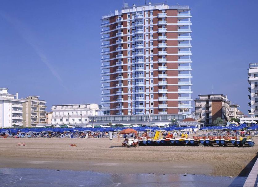 Hotel Caravelle, Jesolo: beachfront high-rise tower behind a sandy beach with umbrellas and loungers