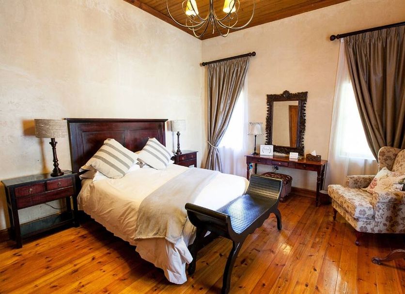 Old House Lodge in Beaufort West guest room with double bed, wooden floors, vanity and armchair
