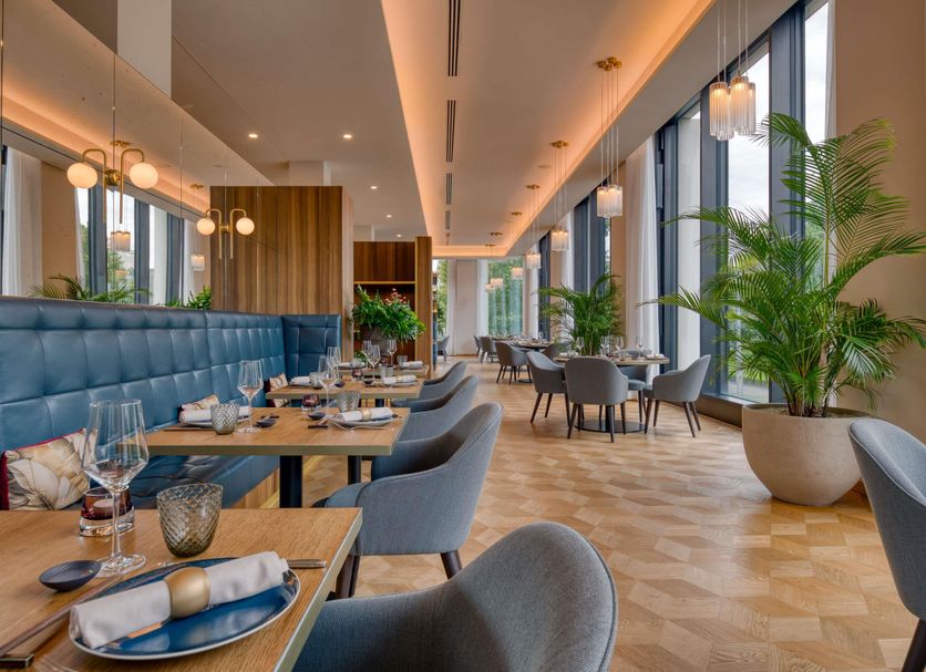 Mövenpick Hotel Basel dining room with large windows, blue banquette seating and potted plants
