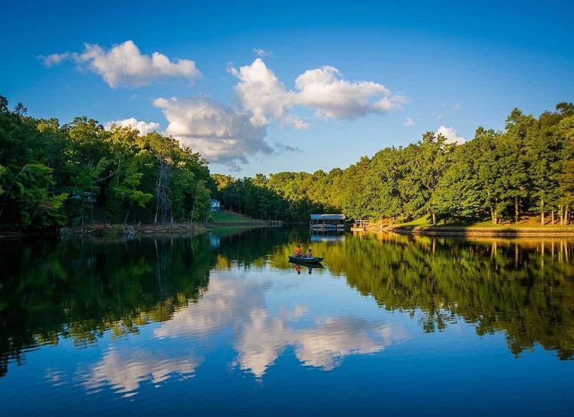 La Quinta Inn & Suites by Wyndham Rock Hill beside a serene lake with trees and cloud reflections