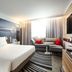 Novotel Narbonne Sud guest room with king bed, sofa seating, wall TV and striped rug in Narbonne