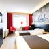 Bastion Hotel Barendrecht room with two beds, red chairs, and cityscape wall mural