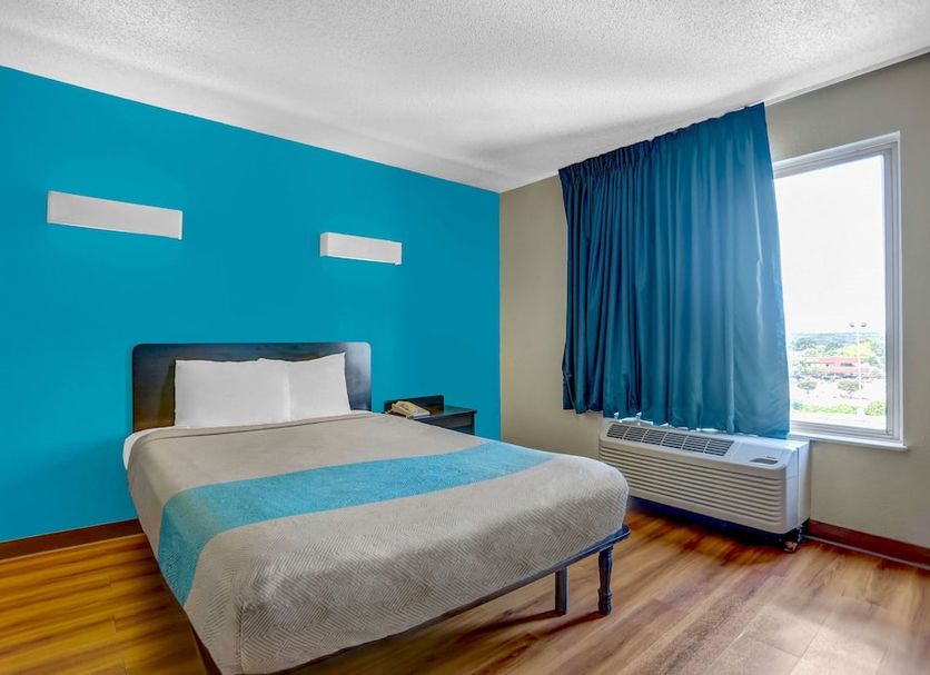 Motel 6 Raleigh North guest room with bed, blue accent wall, window, and air conditioner in Raleigh