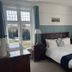 Gwyndra House B&B in St. Austell bedroom with a wooden bed, large windows, and blue curtains.