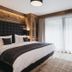 Vaya Sölden guest room with king bed, rustic wood accents and large window with sheer curtains.