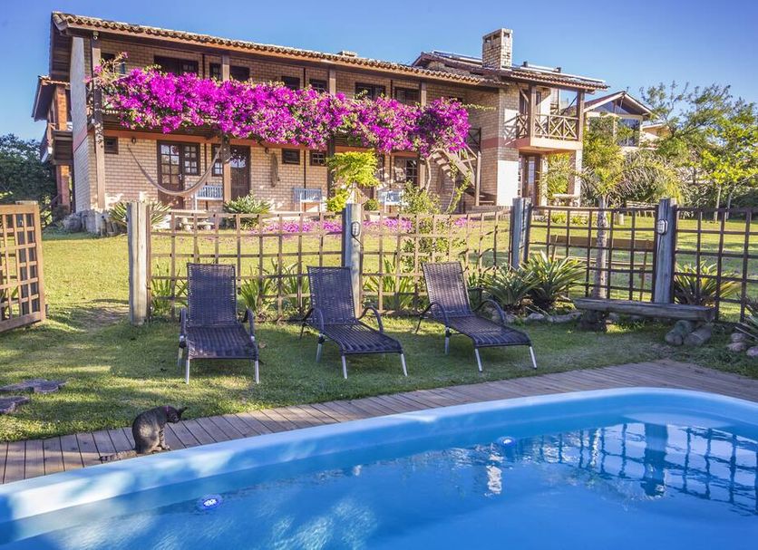 Pousada Capitão Cook in Imbituba with poolside loungers, garden, and flower-covered facade