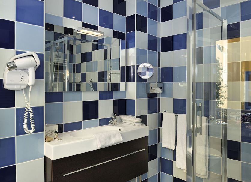 Hôtel de l'Abeille Orléans bathroom with blue checkered tile, sink, mirror, shower and wall hair dryer