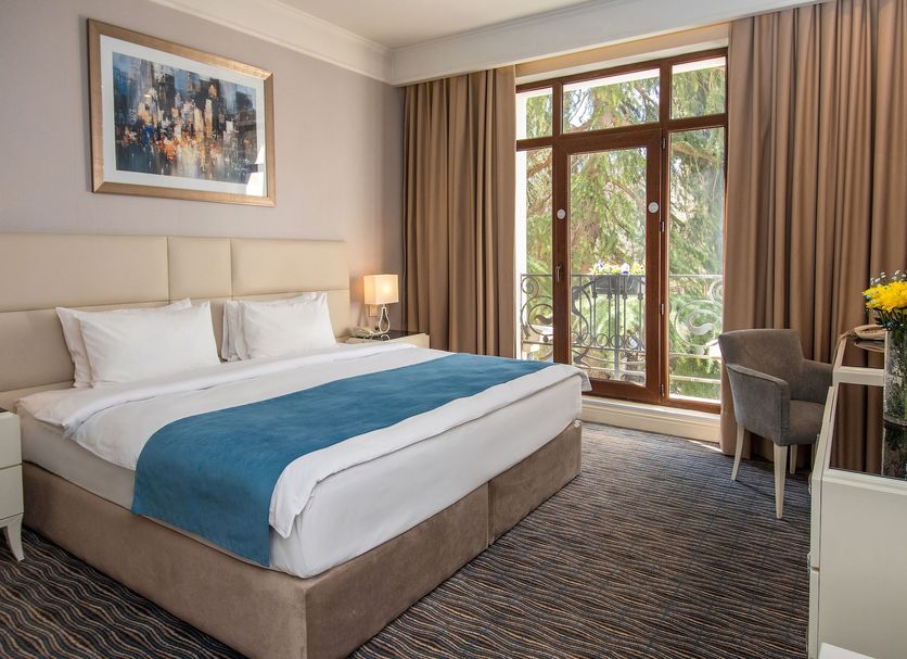 City Avenue Hotel Tbilisi guest room with king bed, desk, armchair, and balcony doors