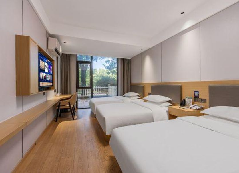 Tizi Hostel in Shanghai twin guest room with three beds, desk, wall-mounted TV, and balcony view