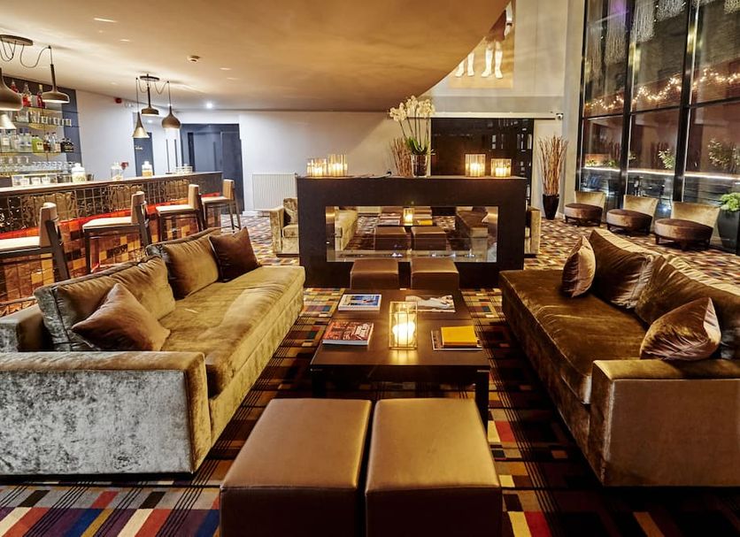 The Augustin Brussels lounge with velvet sofas, central fireplace, bar, and large windows