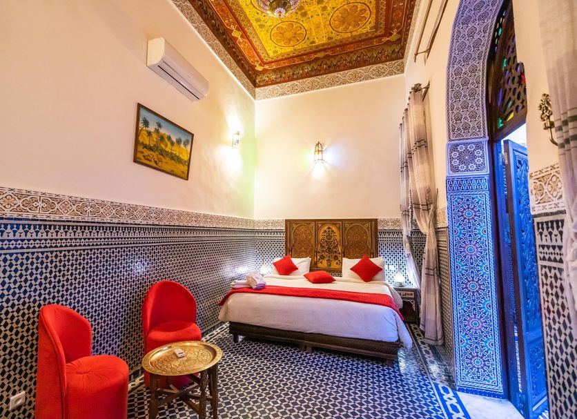 Dar Fes Tresor in Fez: ornate guest room with patterned tile walls, red chairs, and arched doorway