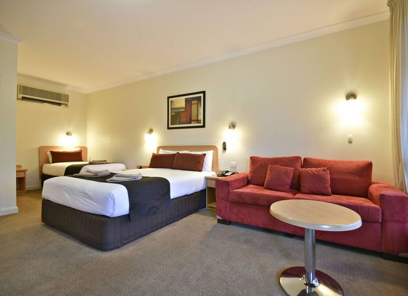 Abel Tasman Motor Inn in Dubbo, twin beds with red sofa and round table in a guest room