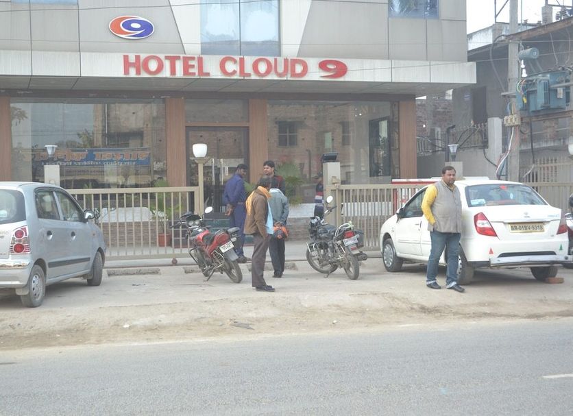 Hotel cloud 9 in Madhubani street view with parked cars, motorcycles, and people outside the entrance