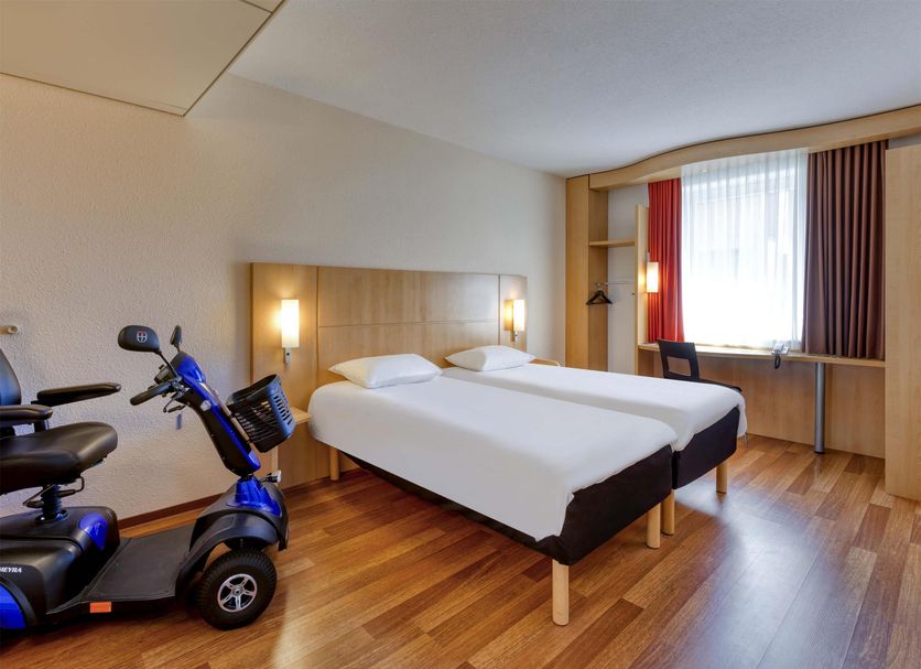ibis Konstanz guest room with twin beds, desk by the window, and a mobility scooter in Konstanz