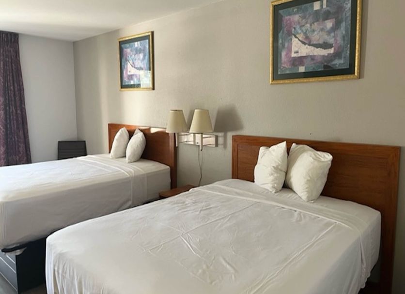 Motel 6 - Laurel, MS guest room with two double beds, wall art, and bedside lamps