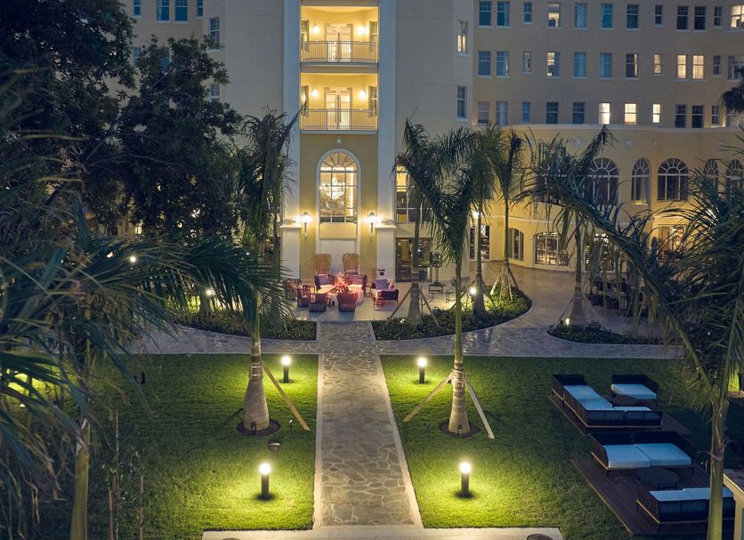 British Colonial Nassau courtyard at night with palm trees, lit walkway, and outdoor lounge seating