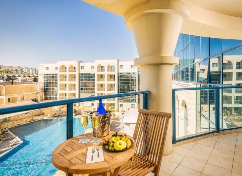 Balcony at The Herbert Eilat with a round table, fruit and drinks overlooking the pool and city