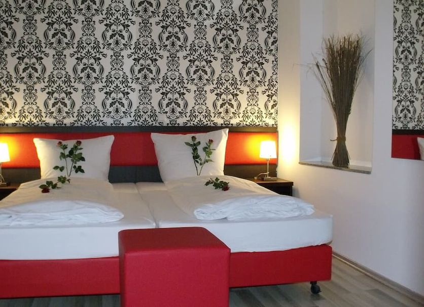 Cityhotel Ahlen Garni in Ahlen: double bed with red headboard and patterned wallpaper in guest room