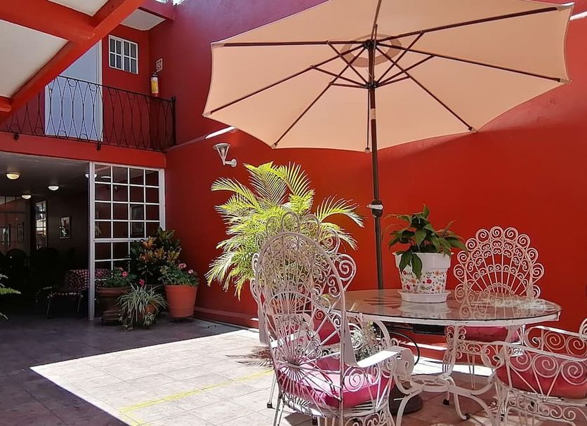Hotel Camba Oaxaca courtyard with red walls, patio table, umbrella and wrought-iron chairs