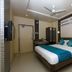 Hotel NavaRATNA, Coimbatore guest room with double bed, teal bedding, ceiling fan, and wall-mounted TV