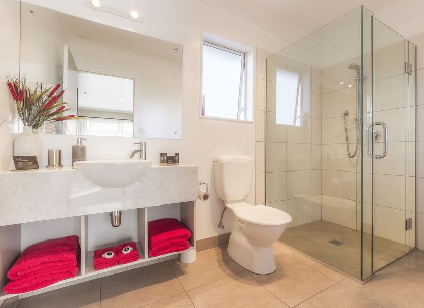Mohua Motels Takaka bathroom with walk-in glass shower, toilet, sink, mirror, and red towels