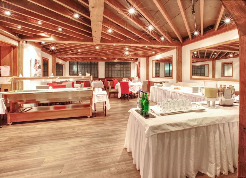 Hotel Alfa in Birsfelden dining room with buffet tables, red chairs, and wood-beamed ceiling